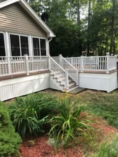 White deck with stairs, built onto a house with beige siding, overlooking a garden.