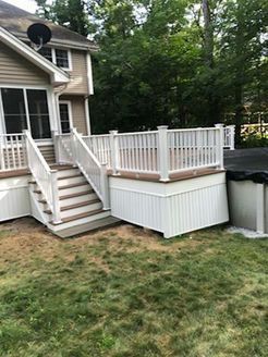 White deck with stairs, built against a house. Surrounding green grass and trees.