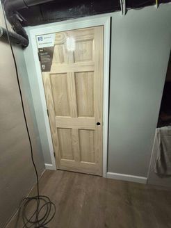 Wooden door with white trim set in gray walls, basement. Black cable in foreground.
