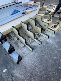Staircase under construction with wood framing and tools, set on concrete ground.