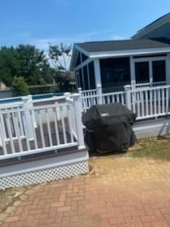 White deck and screened porch next to a swimming pool, grill covered in black.