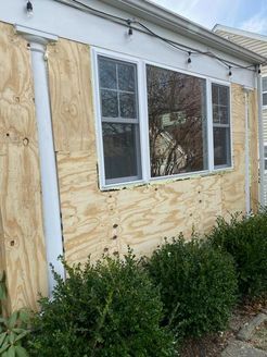 Exterior of a house with plywood covering the siding. Windows are boarded up, and bushes are in front.