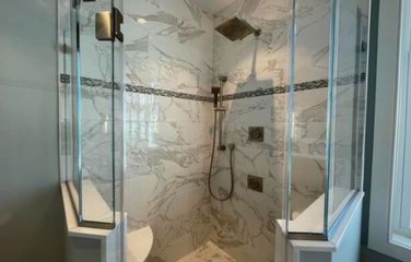 Glass-enclosed shower with white marble walls, a decorative tile stripe, and multiple showerheads.