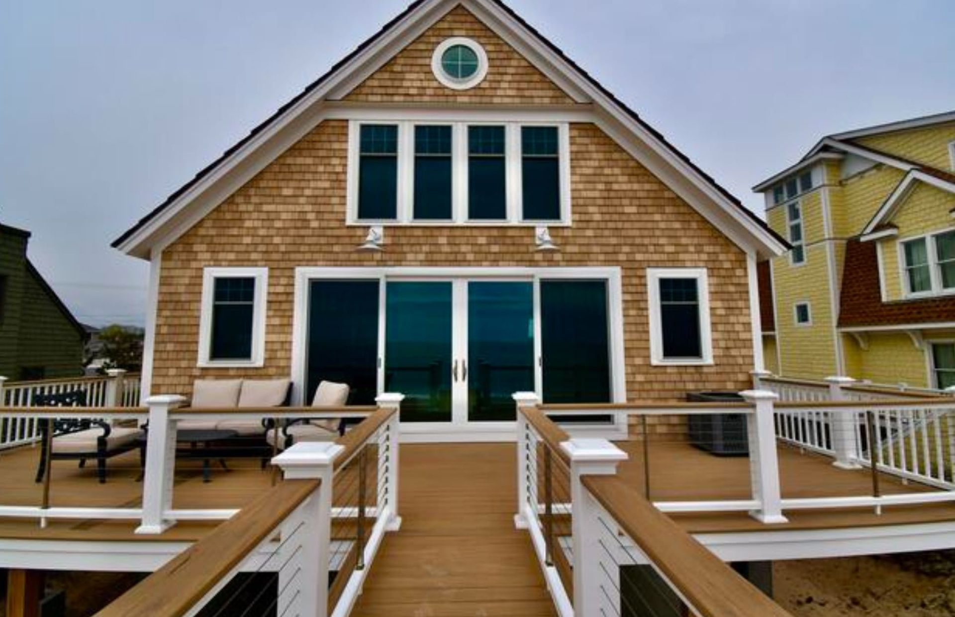 Beach house with wood siding, deck, and large glass doors, facing the ocean.