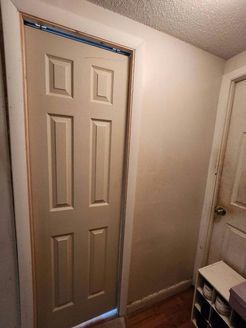 Beige door with six panels in a doorway.  A side wall and a small shelf are visible.