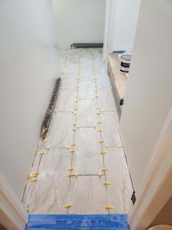 Narrow hallway with light-colored tiled floor, yellow tile spacers, and white walls.