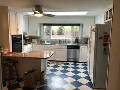 White kitchen with a blue and white checkered floor, island with a granite countertop, and stainless steel appliances.