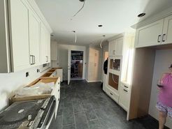 Kitchen under construction; white cabinets, gray floor, open doorway, wire hanging.