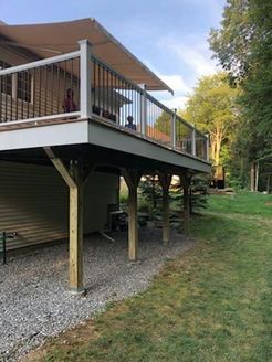 Deck with awning, supported by posts, next to a grassy yard.