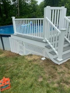 Above-ground pool with white deck and stairs. Gray and white deck materials. Green grass surrounds.