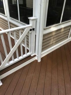 White gate and railing on a brown deck, leading to a screened porch with beige siding.