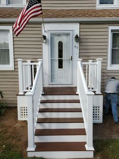 Front entrance of a house with white railings, brown steps, American flag, and a person working on the right.