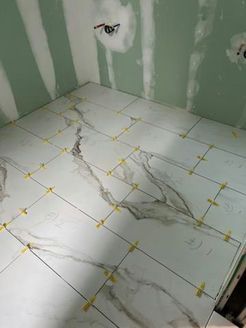 Bathroom floor being tiled, gray veined tiles, yellow spacers, walls are green.