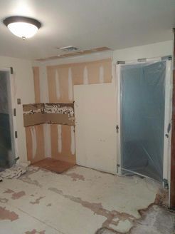 Kitchen undergoing renovation; drywall exposed, floor debris, doorway covered in plastic.