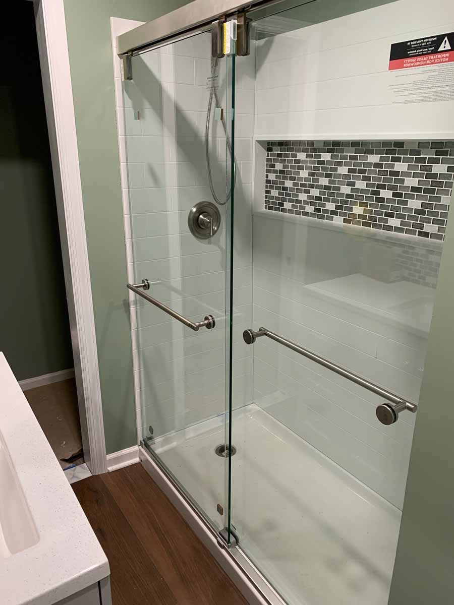 Glass shower with grab bars and mosaic tile accent, set against a light green wall and white vanity.