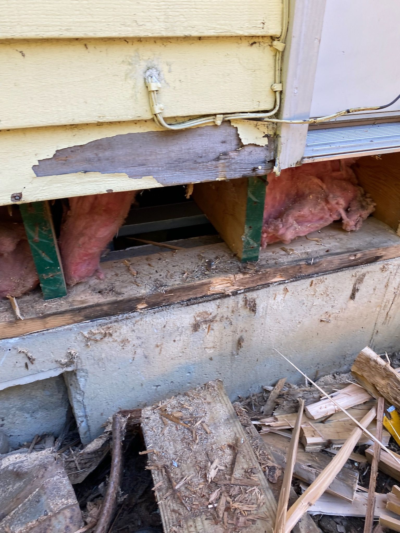 Damaged house foundation with exposed insulation, wood, and concrete.