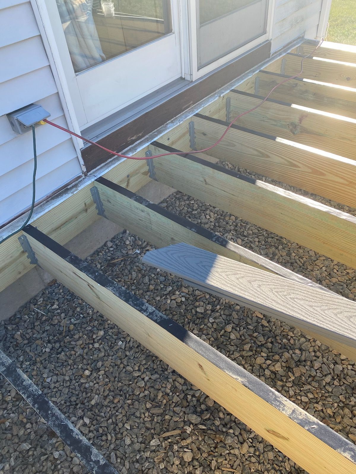 Deck frame under construction with gravel base, near a sliding glass door.
