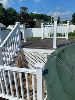 White deck with stairs, railings, and latticework. Dark wooden deck surface near a pool with a green cover.