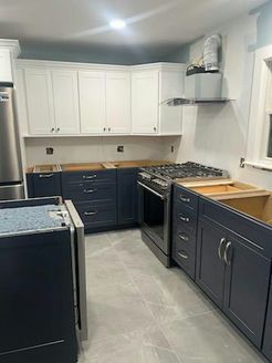 Kitchen renovation with two-tone cabinets: white uppers, navy lowers. Stainless steel appliances and gray tile floor.
