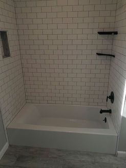 White tiled bathroom with a bathtub, black fixtures, and built-in shelves.