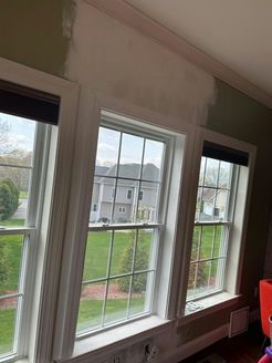 Three white-framed windows in a room with green walls and a patched wall section. Exterior view with green lawn.