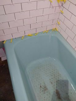 Blue bathtub with white subway tile partially installed. Yellow spacers are visible.