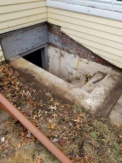 Concrete basement entrance with steps, brickwork, and soil; a weathered look.