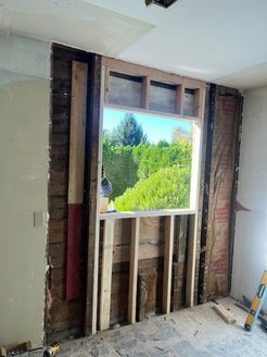 Interior wall with framed window.  Window reveals lush green trees and blue sky. Construction in progress.