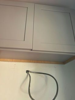 Gray cabinets above a white wall with an electrical cord.