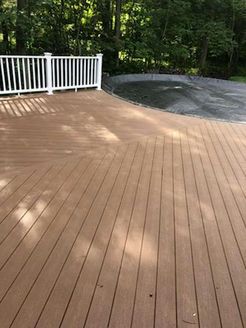 Brown wooden deck with white railing, overlooking a pool covered in a dark tarp, set in a wooded area.