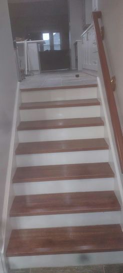 Staircase with wooden steps and white risers, leading to a hallway.  Handrail is present.