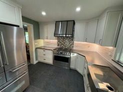 Modern kitchen with stainless steel appliances, light gray cabinets, dark countertops, and tile backsplash.