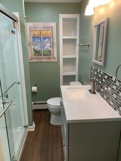 Bathroom with green walls, glass shower, white vanity, and artwork of a window.