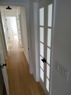 Hallway with white walls, light wood floor, and multiple doors. Frosted glass door on right.