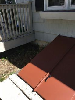 Brown basement door at house corner, beside a wooden deck and white foundation.