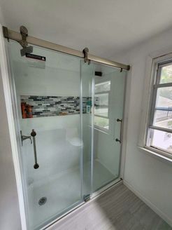 Glass shower with sliding door, stainless steel hardware, and decorative tile accent. Next to a window.