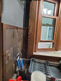 Kitchen sink area with copper-colored wall paneling, wooden window trim, and a window overlooking a yard.