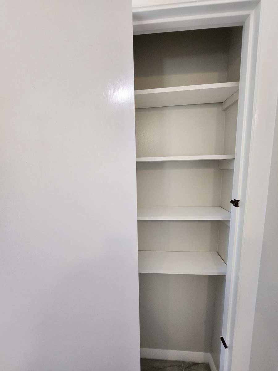 White shelving unit inside a white door frame. The shelves are empty.