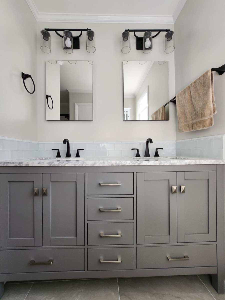 Gray bathroom vanity with two sinks, mirrors, and sconce lighting.