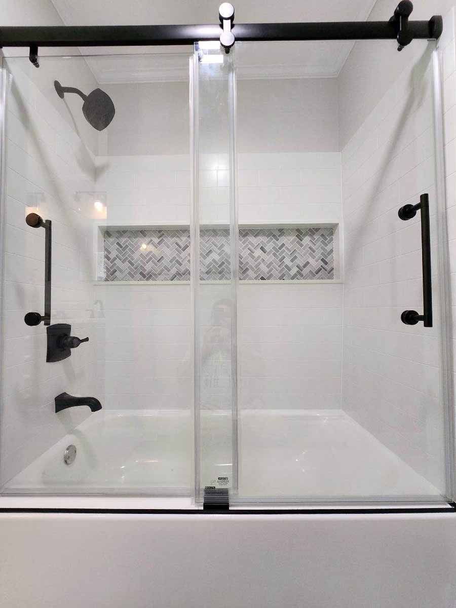 White tiled shower with glass sliding doors, black hardware, and a built-in shelf.