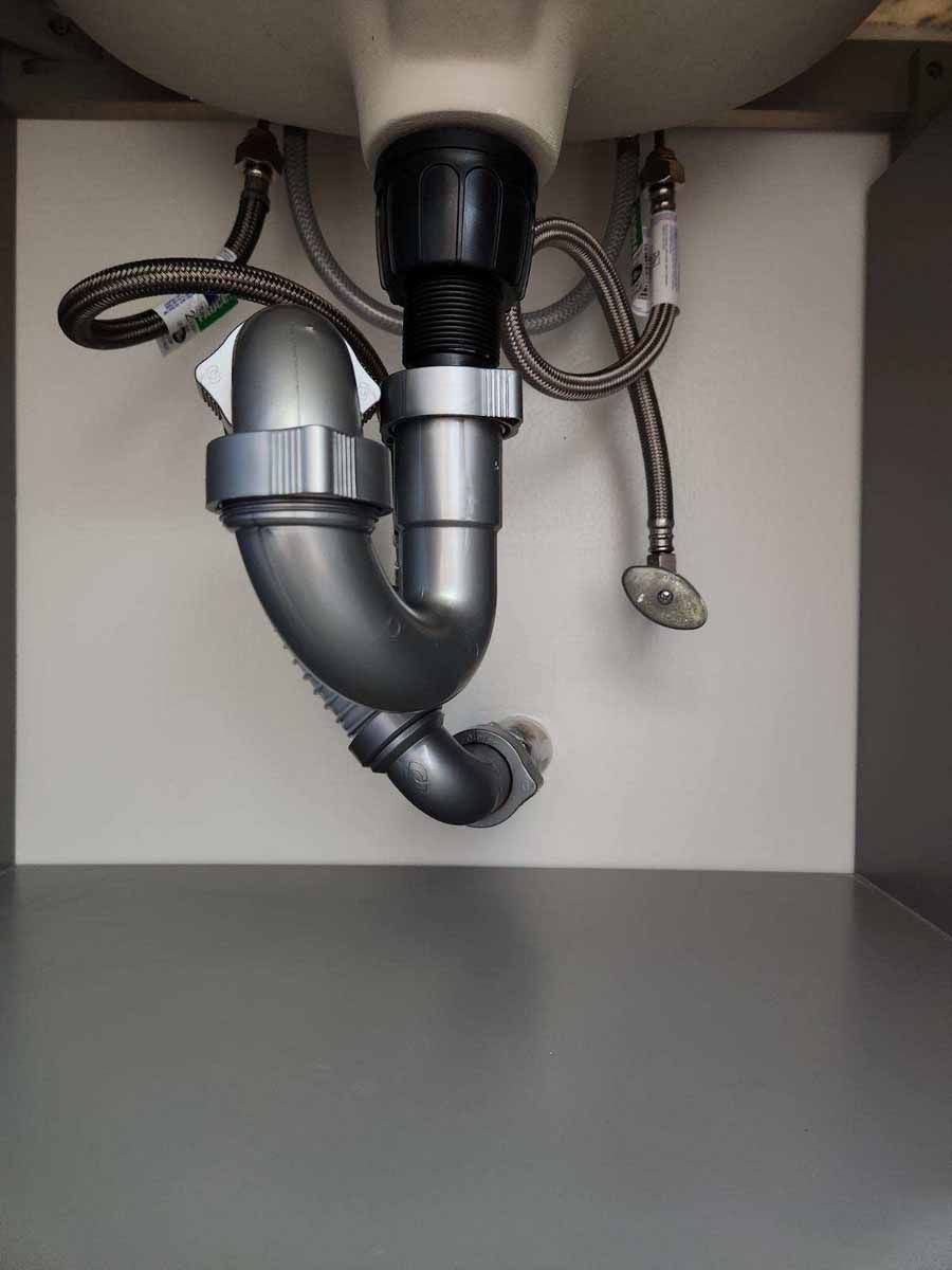 Plumbing under a white bathroom sink with a gray P-trap and supply lines.