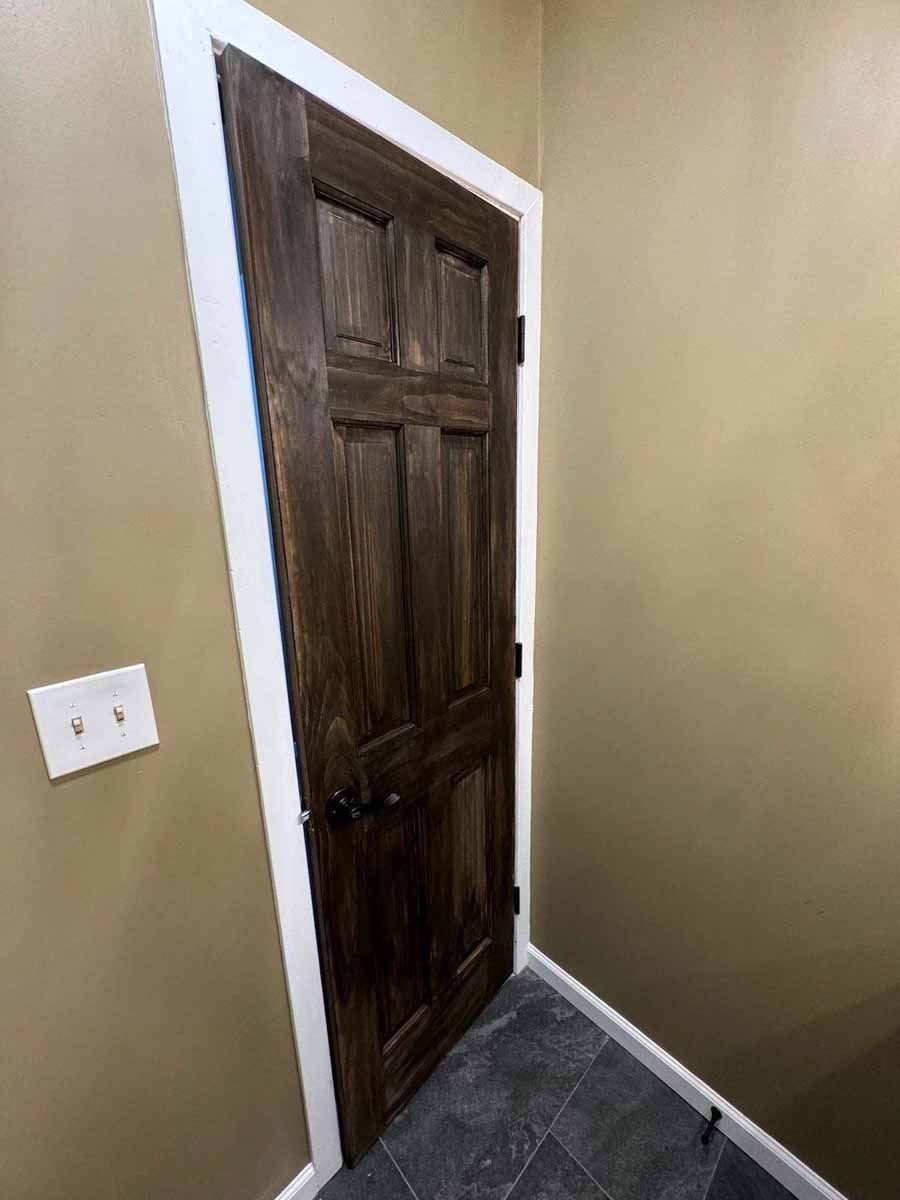 Dark brown paneled door with white trim, on a tan wall. Floor is dark tile.