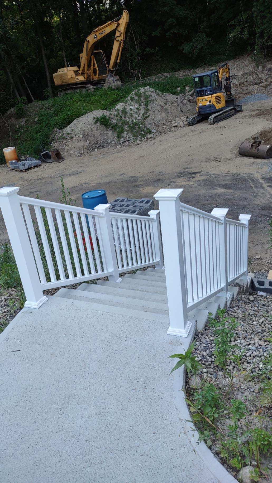 Concrete stairs with white railing leading uphill to construction site with excavators.