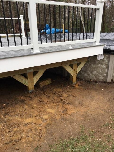 Wooden deck supported by posts and braces over dirt.