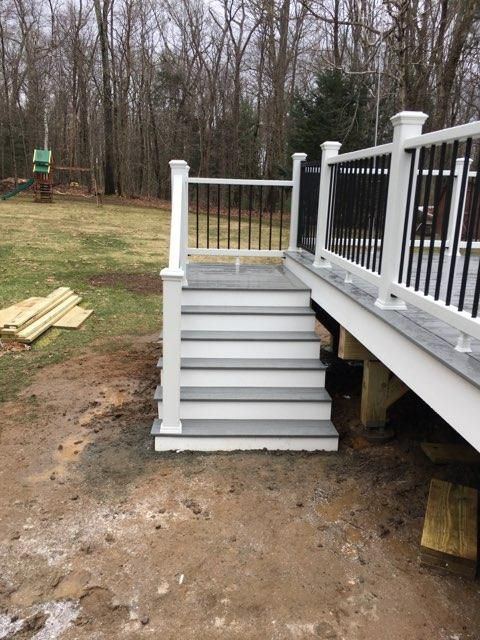 A gray and white deck with stairs, black railings, and a backyard setting.