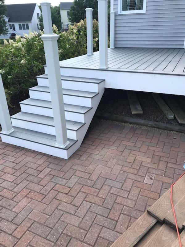 Deck with white stairs and railings, leading down to a red brick patio.