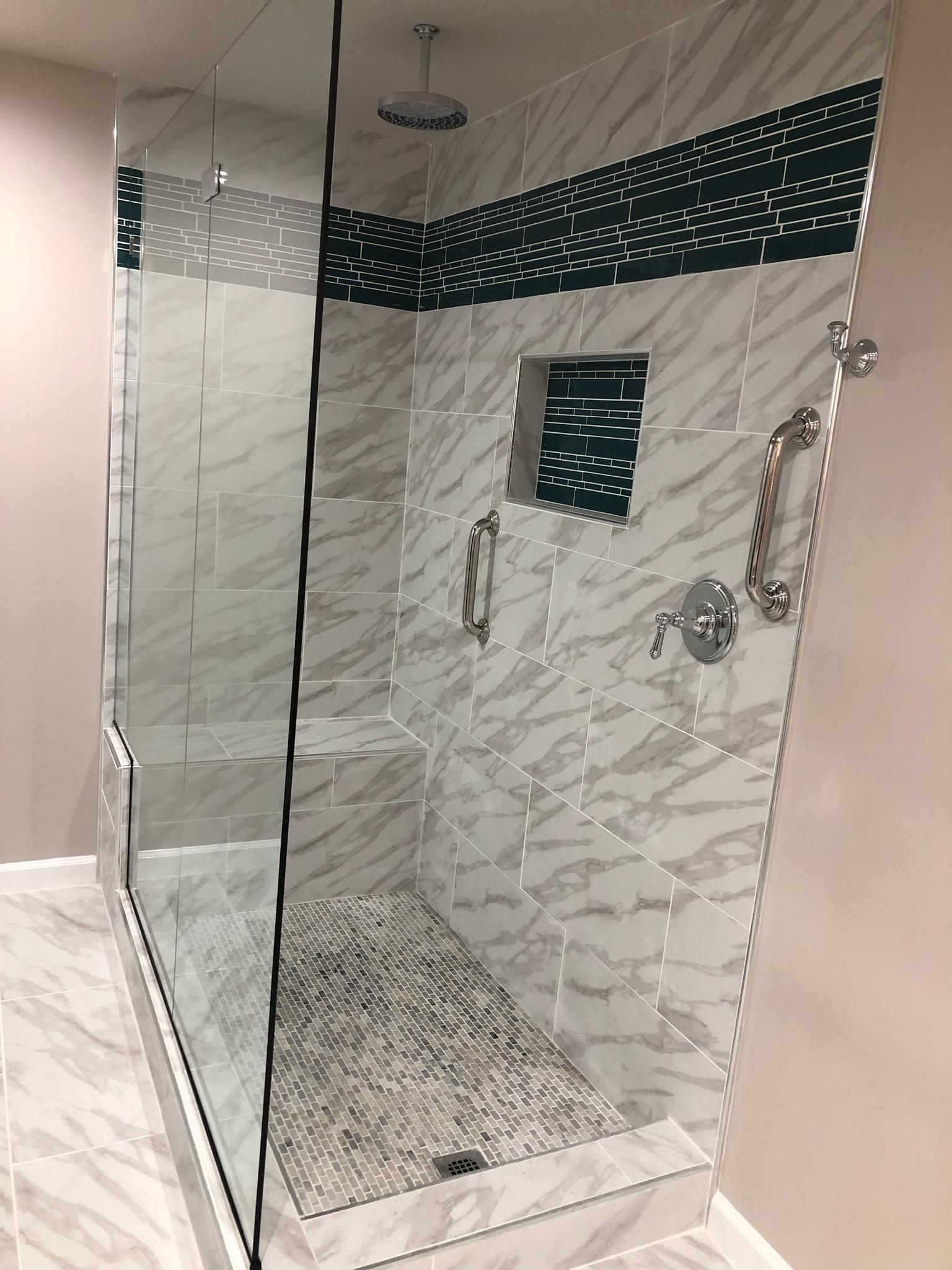 Modern shower with glass door and marble tile. Dark green accent, silver fixtures.