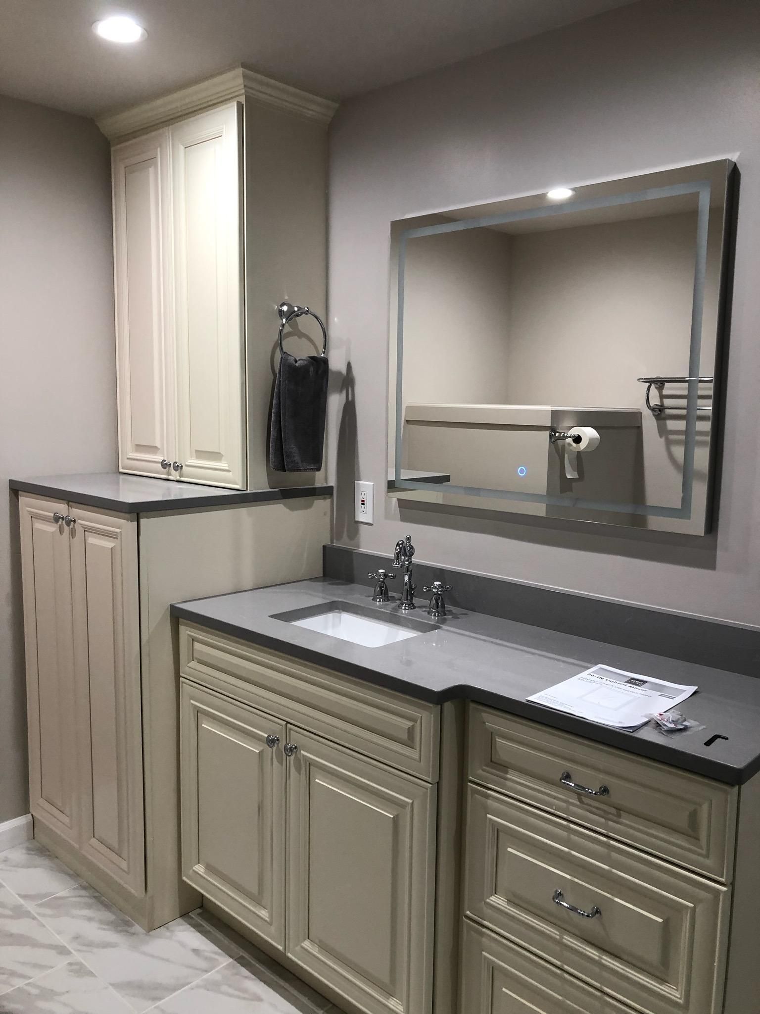 Bathroom with light cabinets, gray countertop, square mirror, and towel rack.