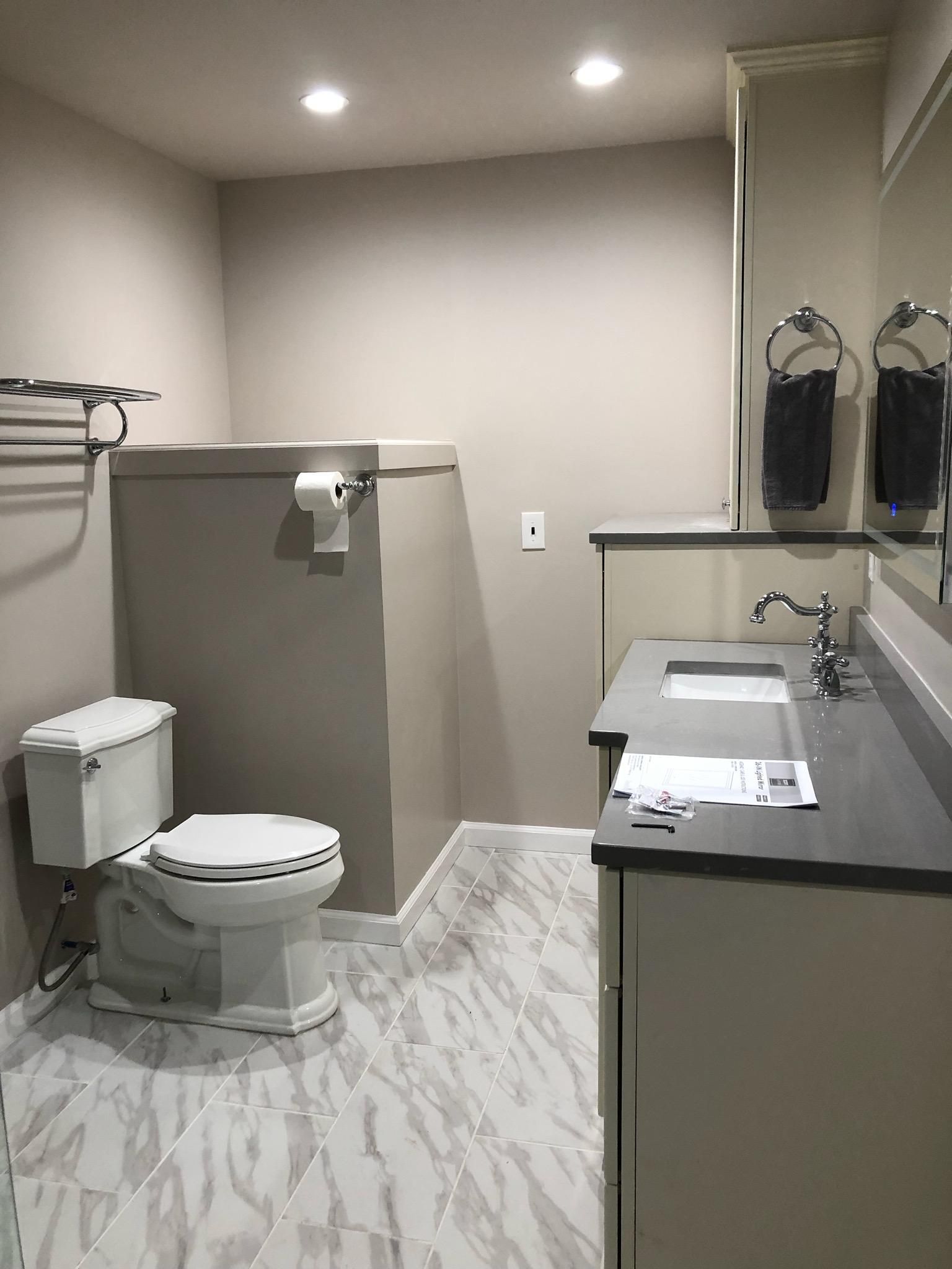 Bathroom with toilet, vanity, and a large, enclosed structure, possibly concealing plumbing. Neutral tones, tile floor.