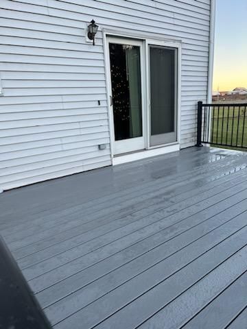 Gray deck with sliding glass doors, black railing, and white siding.
